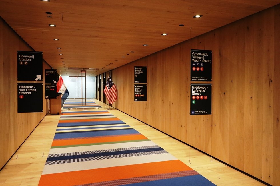US and Dutch flag flank the glass entry into the natural wood entry gallery outfitted with a long custom woven rug and subway signs in Dutch and English